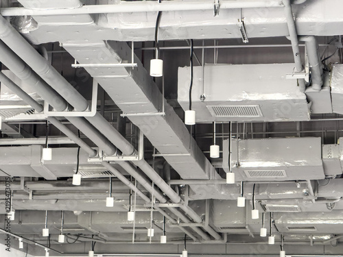 Obraz na plátně Modern Industrial Ceiling with Exposed Pipes and Lighting Fixtures in a Contempo