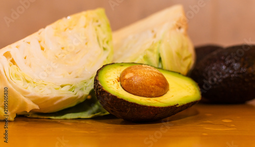 Canvastavla Medio aguacate con carozo en primer plano, con trozos borrosos de col verde fresca en el fondo desenfocado