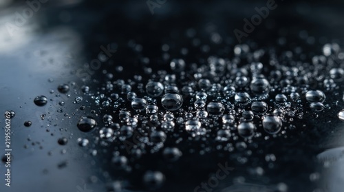 Macro photography of clear water droplets on a smooth dark reflective surface.