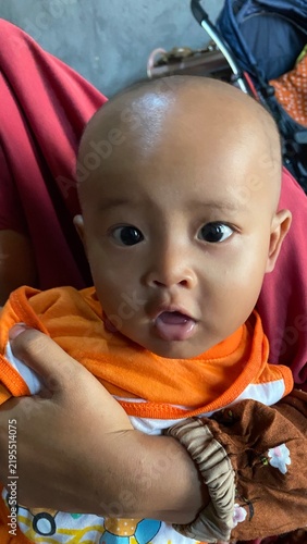 Close-up portrait of a curious baby boy with wide eyes, wearing an orange shirt and being held