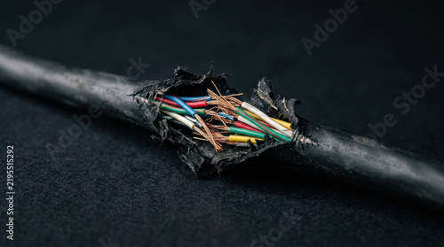 Damaged cable with exposed copper wires and insulation on dark background showing micronutrient deficiency in material quality and wear