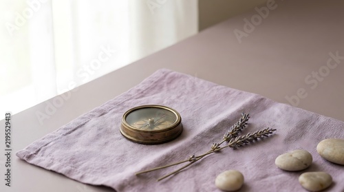 Vintage brass compass resting on soft pink fabric with dried lavender sprigs and smooth stones