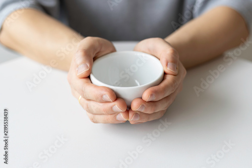 Close-up of a person holding an empty white ceramic cup with both hands at a table