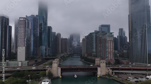 Aerial View of Chicago River and Downtown Skyscrapers Under Foggy Sky” An aerial view of the Chicago River winding through downtown, flanked by high-rise buildings and a historic drawbridge, 
