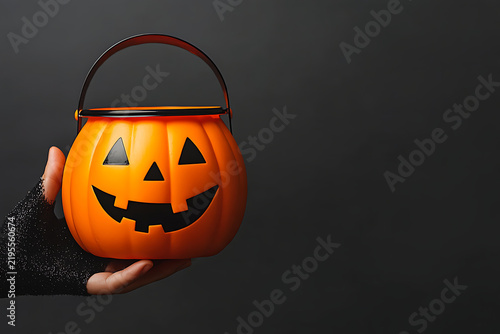 Dark cinematic close-up of hand holding glowing pumpkin bucket with right copy space for luxury Halloween party invitation