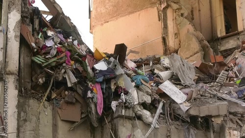 Close-up view of a destroyed high-rise residential building in a Ukrainian city after a Russian drone strike. Concrete fragments mixed with household belongings and furniture are visible through a