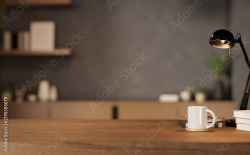 Close up of wooden desk with white mug, lamp and books in blurred modern office background.