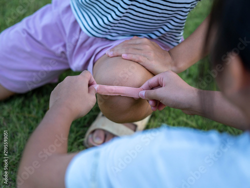 Close-up of girl applying adhesive plaster bandage to her younger sister injured scraped knee outdoors