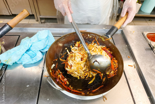 A chef is cooking fettuccine with a vegetable mix in a hot frying pan.