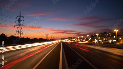 Highway traffic streaks at dusk with power lines and city lights