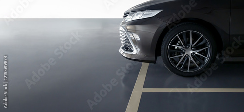 dark grey sedan front quarter view, multi-spoke alloy wheel, sleek headlight, glossy bumper, parked on reflective studio floor, cream-colored lines, parking lot, anti slip coating floor for safety
