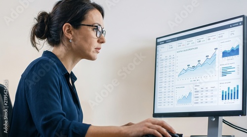 Businesswoman analyzing financial data charts and graphs on computer screen in office