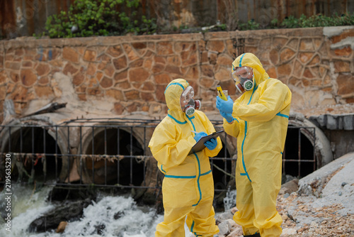 Принти на полотні Two field workers wearing protective suits check water testing results, comparing measurements and recording data near drainage outlet