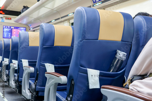 Blue and beige train seats line a modern carriage. Empty seats suggest quiet travel or waiting. Water bottle rests in a tray pocket. Clean, orderly design reflects comfort and efficiency
