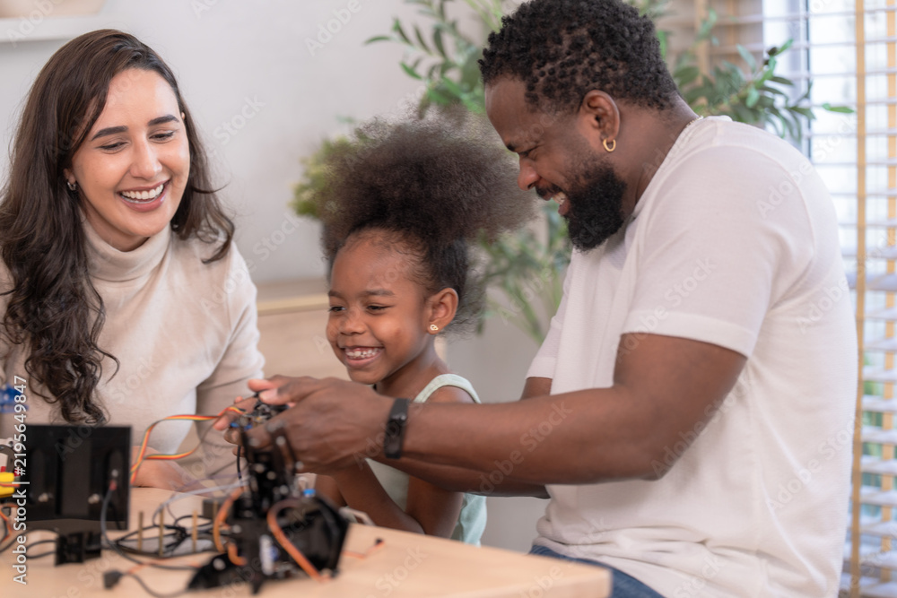 Fototapeta premium A close family of three explore a blue robotic arm together by a window with green plants, celebrating learning together with a clean modern aesthetic perfect for family and lifestyle.