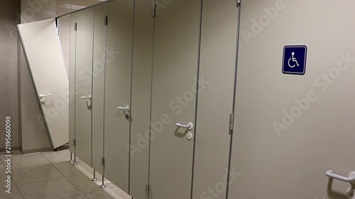 A row of doors toilet in the public restroom with the devastated door of the last cabin.