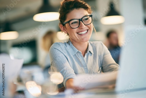 Smiling young woman with glasses working on a laptop computer in a modern bright office space