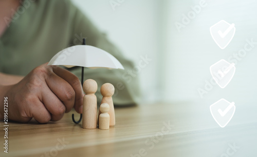 Cuadro en lienzo Concept of family insurance protection with wooden doll figures under small umbrella and safety checkmark icon