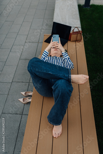 Фотография Woman relaxing on bench checking smartphone
