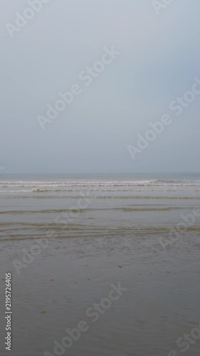 Calm ocean waves washing over a sandy beach on a foggy, overcast day. Serene and tranquil seascape background.