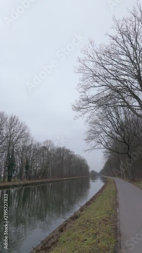 Serene POV walking shot along a canal towpath with bare winter trees on an overcast day.