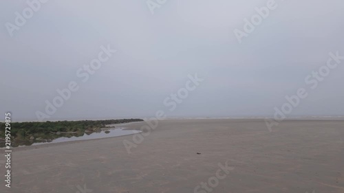 Slow drone flight over a vast, empty beach on a foggy, overcast day
