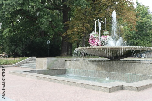 Stone fountain with floral arrangements in a lush park.