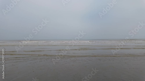 Calm and moody seascape with gentle waves rolling onto an empty, foggy beach.