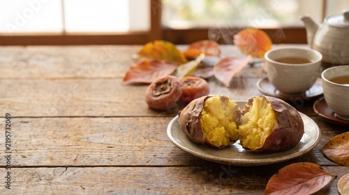 Obraz na płótnie 木の板の上に置かれた丸ごとと断面の焼き芋と散りばめられた紅葉