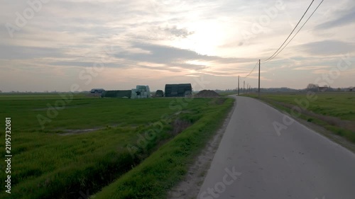 POV journey on an empty asphalt road through green fields in the rural landscape at dusk.