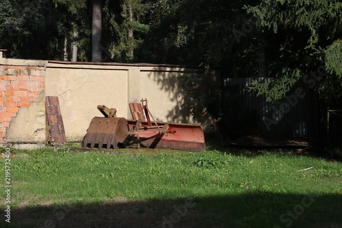 Vintage rusty snow plow leaning against a concrete wall.