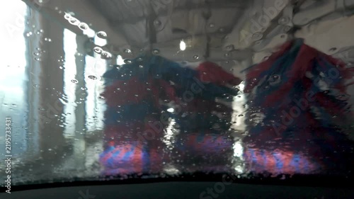 POV of a car moving through an automatic car wash tunnel with rotating brushes and water on the windshield.