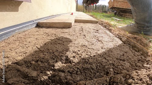 Worker Aligns Concrete Paving Slab on Sand Bed Beside Building