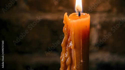 Burning orange wax candle with melting drips in dark room