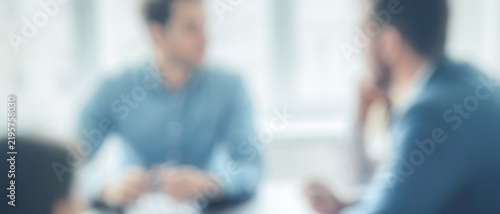 A blurry image of a business meeting with individuals engaged in discussion. Focus is on the interaction among participants in a professional setting.