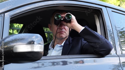 Man in car using binoculars for covert surveillance outdoors