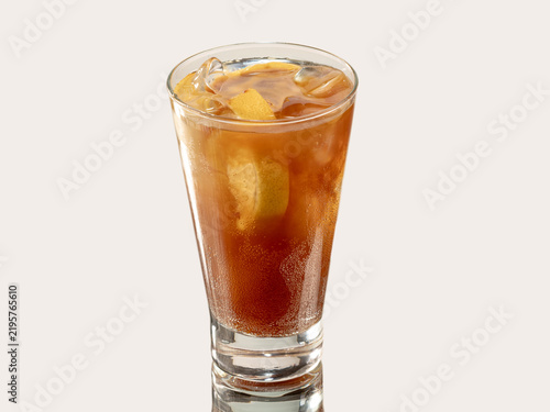 Tall glass of dark iced tea with a lemon slice and ice cubes, shot on a light neutral background.