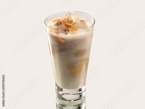 Tall glass of iced coffee with milk and caramel swirl, topped with ice cubes, shot on a light background.