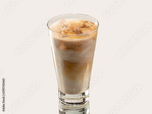 Tall glass of iced coffee with milk and caramel swirl, topped with ice cubes, shot on a light background.