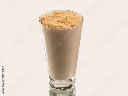 Tall glass of rich chocolate smoothie topped with banana slices on a skewer, shot on a light neutral background.