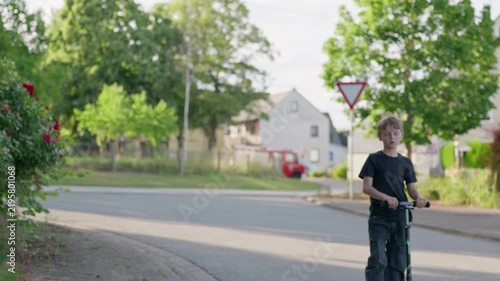 Unrecognizable boy riding kick scooter in village along a quiet residential street in a rural village on a sunny summer day