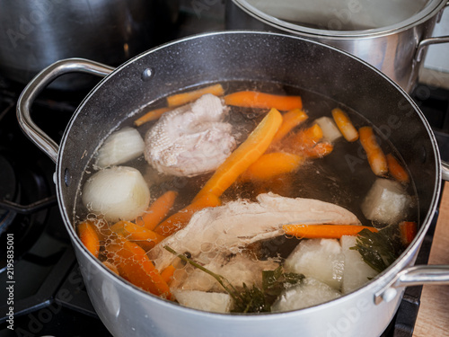 Картината върху платно Homemade chicken broth cooking in a large pot with chicken meat, carrots, onion and root vegetables, showing traditional soup preparation on a kitchen stove