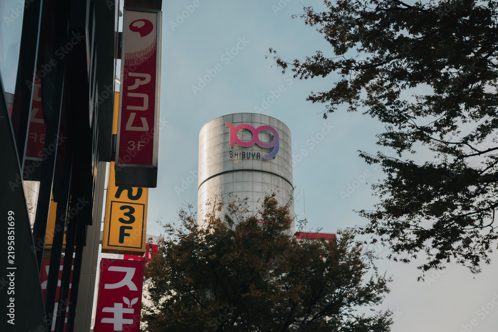 Obraz premium SHIBUYA, TOKYO JAPAN - NOVEMBER 16, 2023: 109 building stands prominently in background behind signage and trees in Shibuya, Tokyo