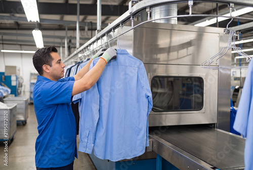 Laundry Technician Hanging Fresh Blue Shirts On Automated Overhead Conveyor System