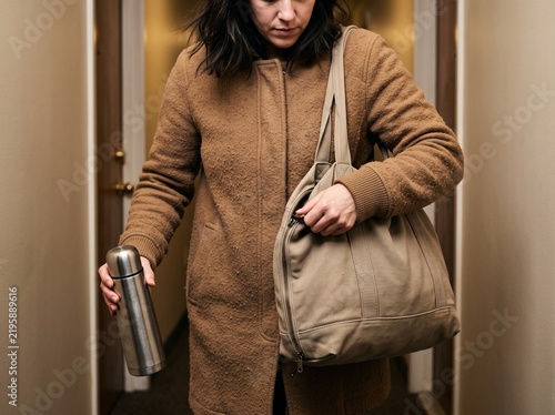 Woman in a brown winter coat packing a thermos into her canvas bag before leaving home