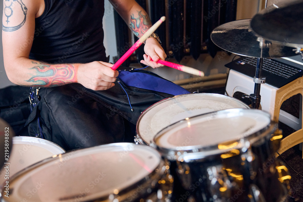 Fototapeta premium Tattooed adult man drumming during rehearsal with vivid pink sticks