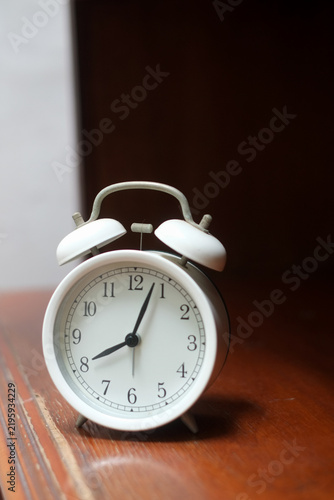 Classic white twin bell alarm clock showing on a wood table with contrast light and shadow background for time management concept.