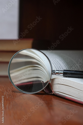 Book and magnifying glass on wooden desk. Searching for Knowledge with Books Concept.