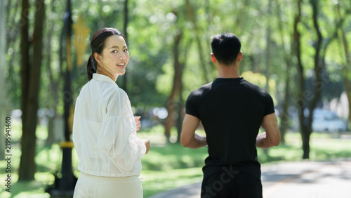 Принти на полотні Asian woman turning back to smile while jogging with partner in park