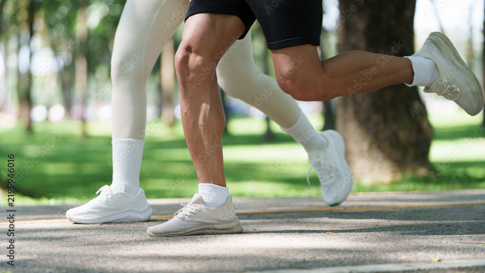 Obraz premium Cropped view of couple legs running together in park for outdoor fitness